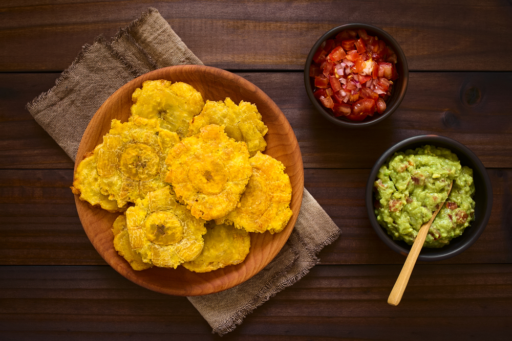 Patacon ou toston fritos e pedaços achatados de banana-verde, lanche tradicional ou acompanhamento no Caribe, salada de guacamole e tomate, cebola